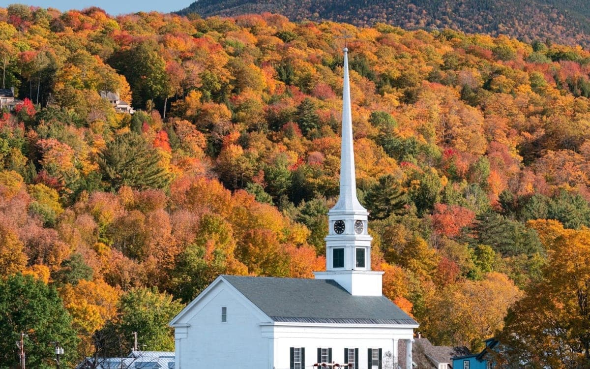 White church steeple in Stowe, Vermont, against hillsides of red and orange autumn trees