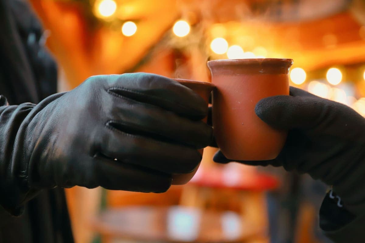 Two people in gloves clinking terracotta Glühwein mugs at a lit European Christmas market stall at night
