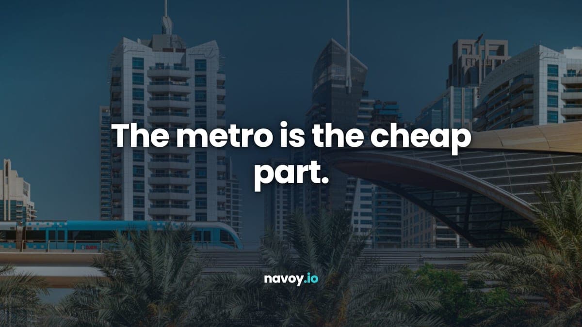 A Dubai Metro train crossing an elevated viaduct past a station canopy with Marina towers behind