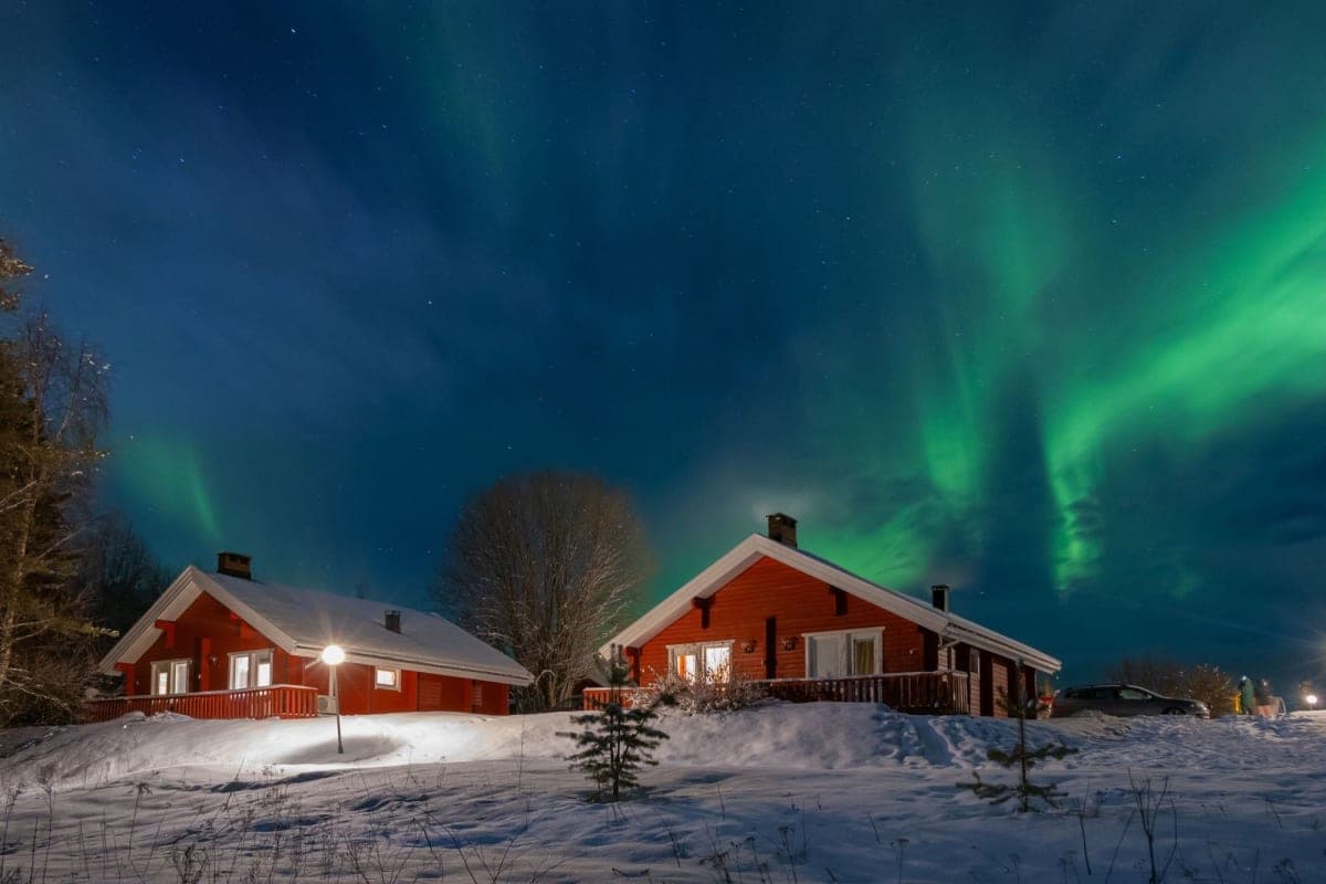 Red wooden cabins under the northern lights in Finnish Lapland
